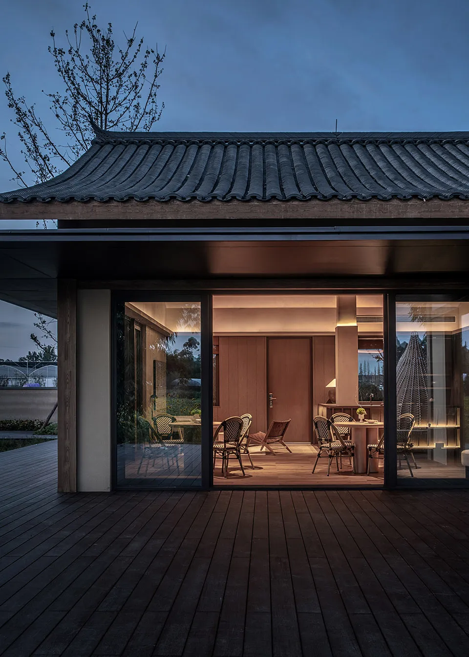 A traditional-style outdoor dining area with dark wooden flooring and a wooden roof, illuminated at dusk.