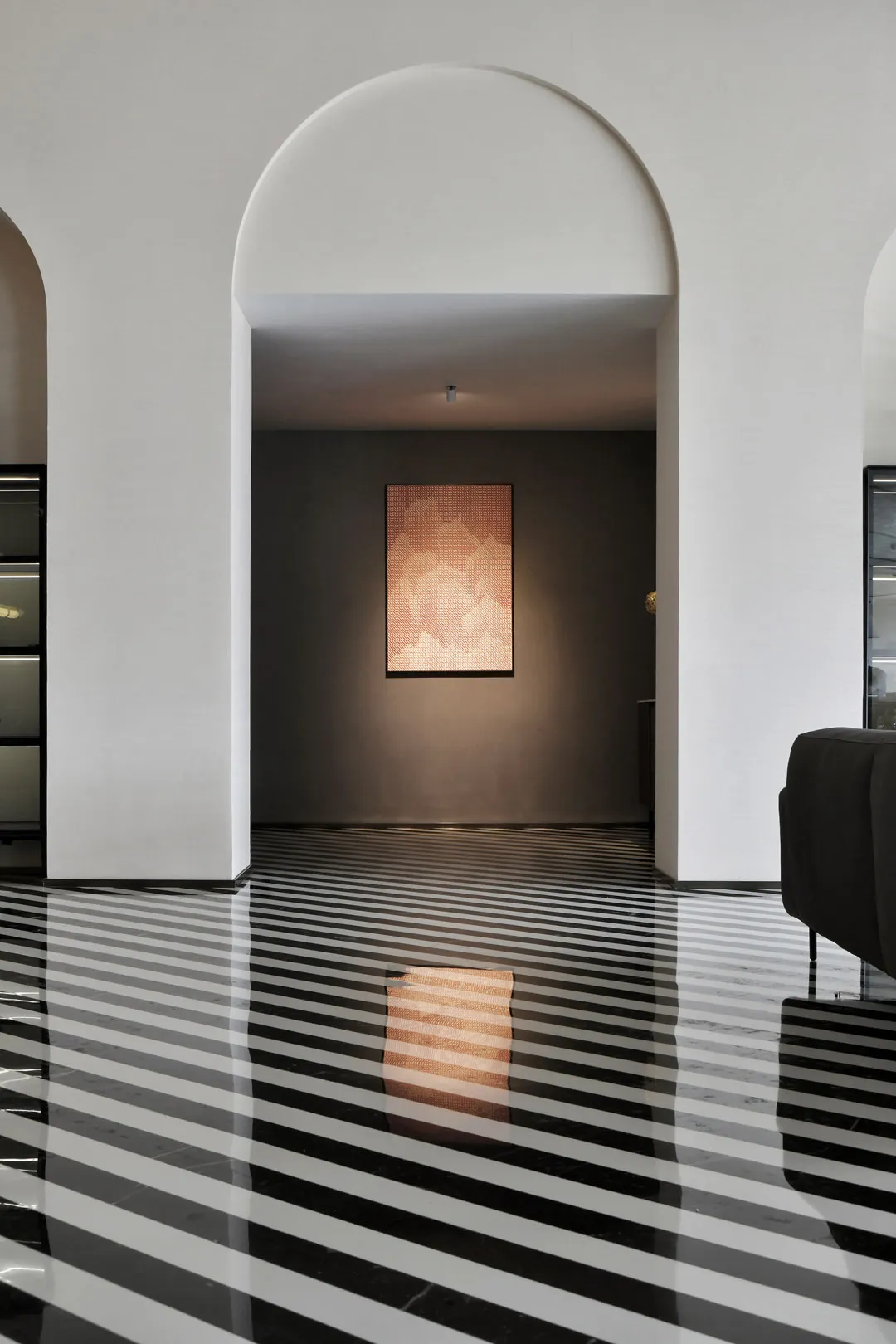 A modern living room with a striped tile floor and an archway leading to a darker room with a lit artwork.