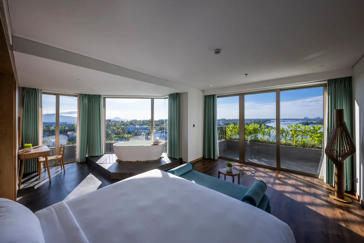 Modern bedroom with black flooring, leather seating, and floor-to-ceiling windows overlooking a scenic view.