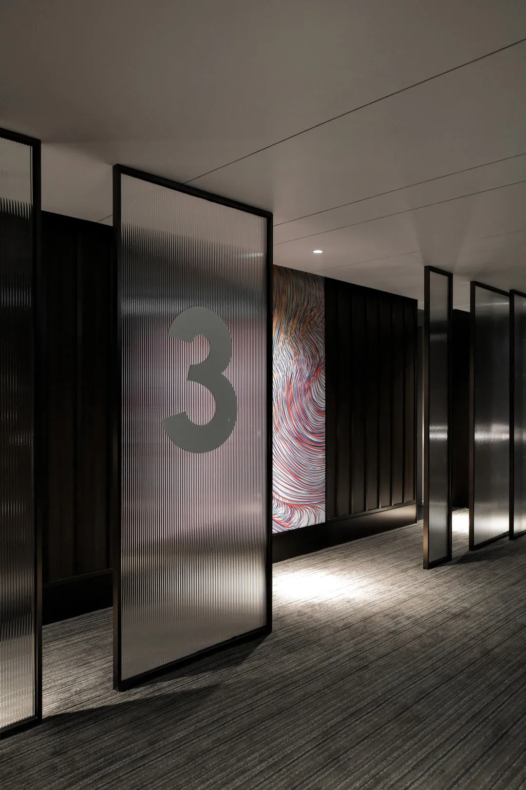 A modern hotel corridor with glass dividing panels and ceiling lighting.