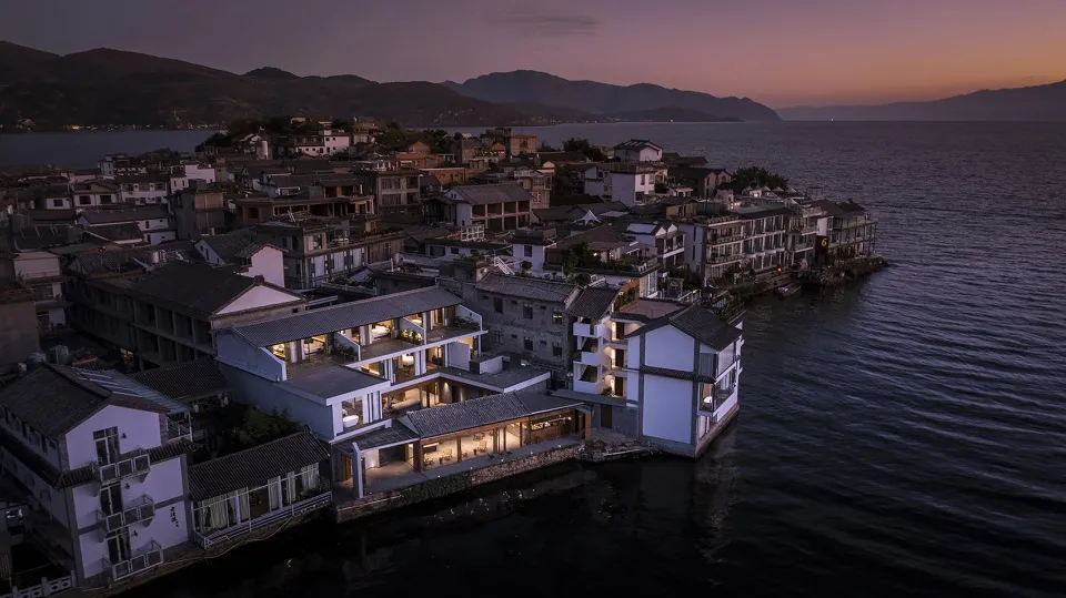 Aerial view of a beachside villa at dusk, featuring traditional architectural elements, illuminated windows, and a serene wat