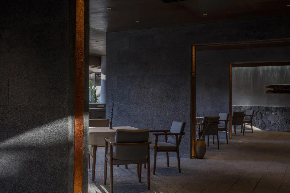 A modern restaurant interior with concrete walls, minimalist furniture, and industrial lighting.