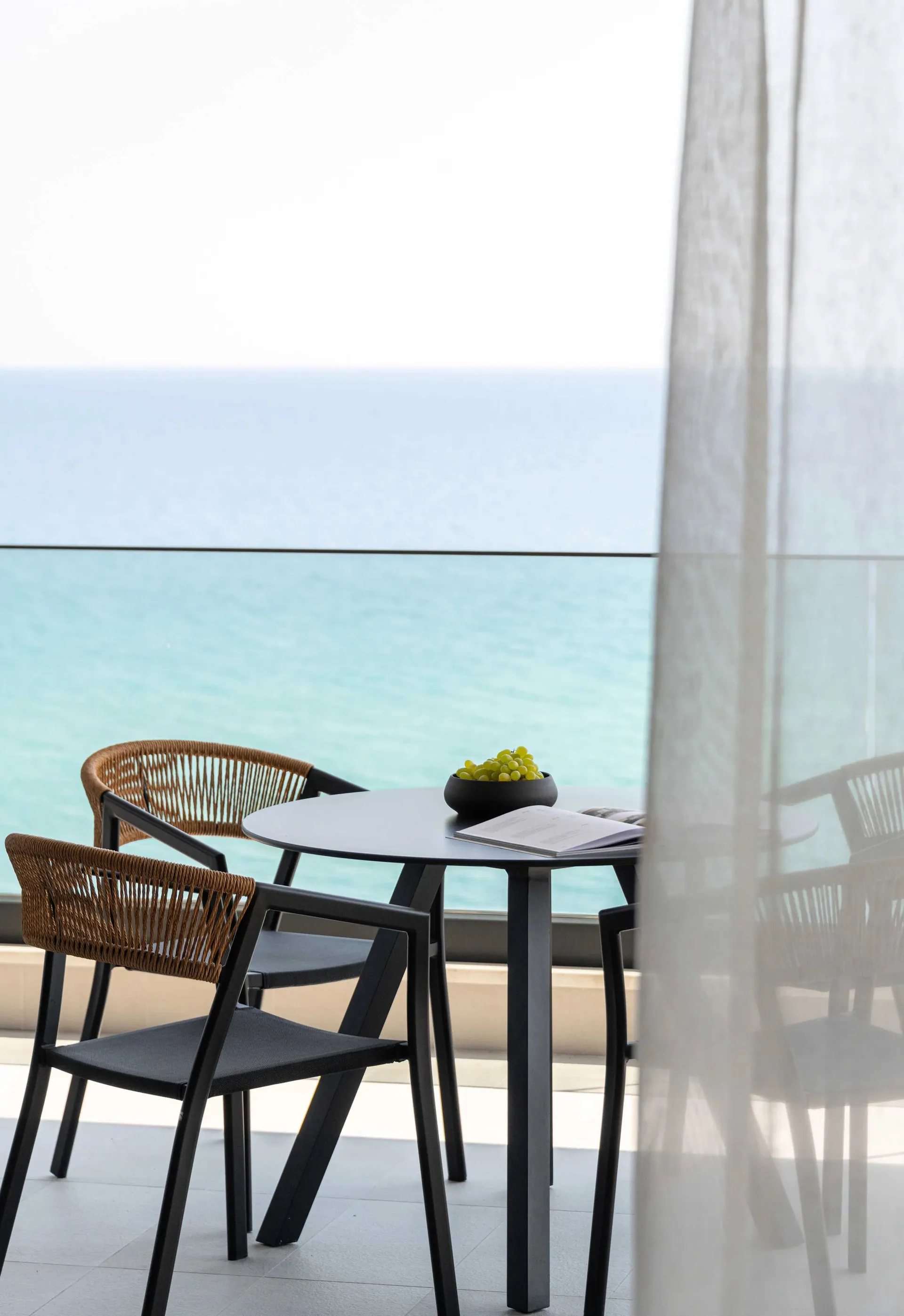 A modern residential balcony featuring metal-woven furniture, overlooking the ocean.