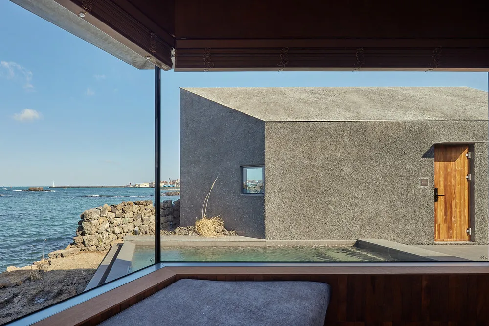 A minimalist concrete house exterior overlooking the ocean with a small pool and stone wall.