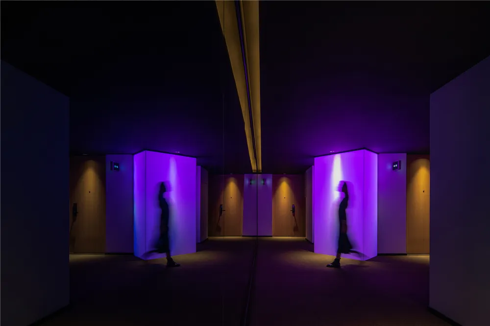 Minimalist corridor illuminated by purple and yellow lights, featuring translucent plastic or plexiglass walls.