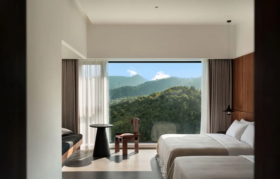 Modern, minimalist bedroom with wooden furniture and a scenic view of mountains through a large window.
