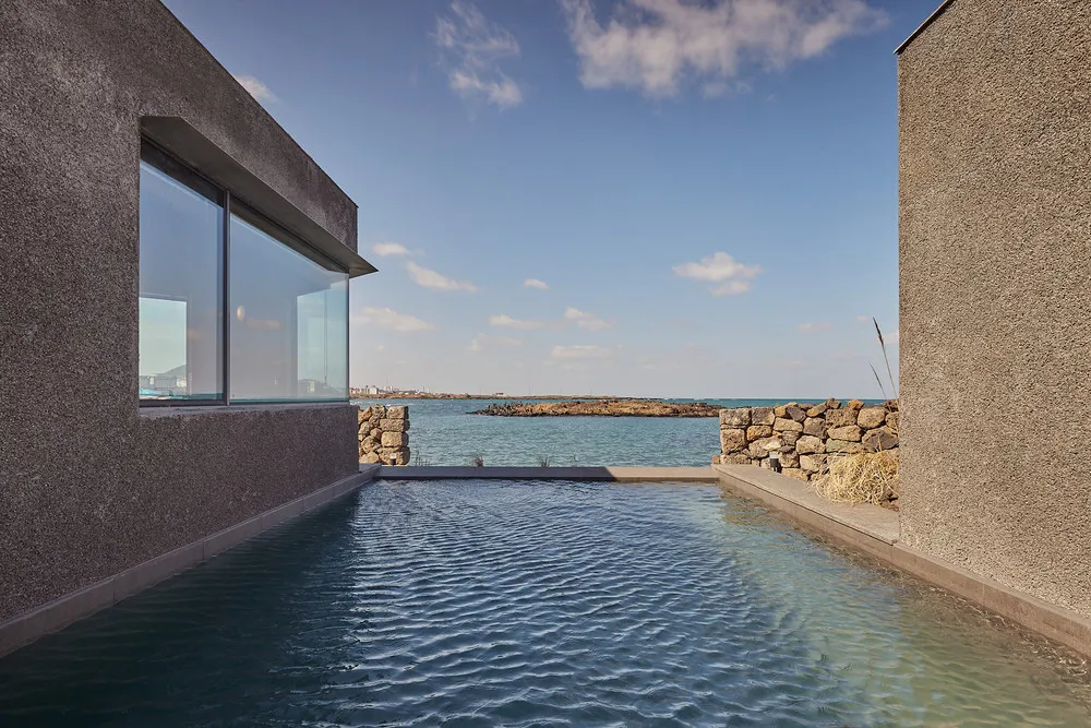 Modern residential pool with concrete and glass walls overlooking the ocean.