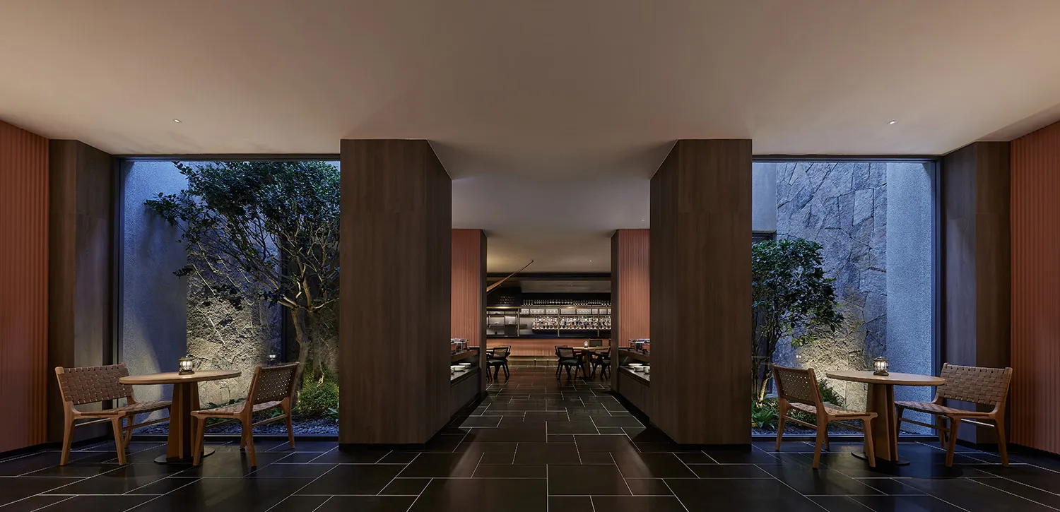 A modern restaurant interior with dark tones, wooden tables, chairs, and stone walls.