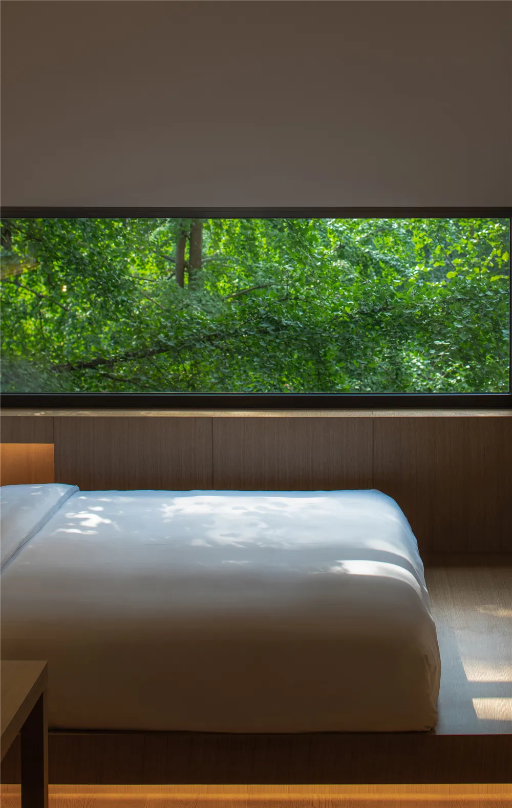 Modern bedroom with a zen-like atmosphere, featuring a bed surrounded by wooden walls and a large window with a view of lush
