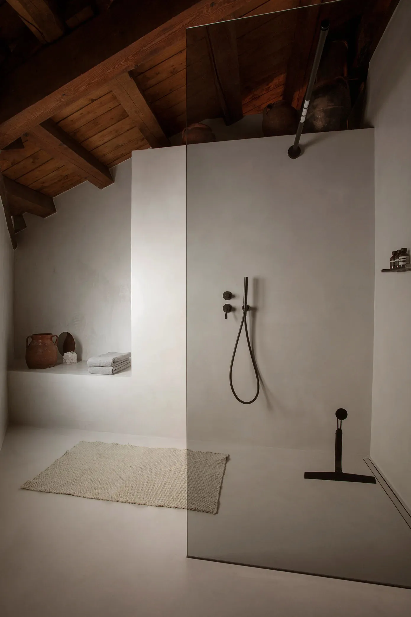Minimalist bathroom with concrete walls and floor, featuring a walk-in shower with a glass door.
