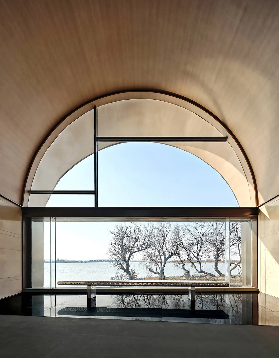 Modern minimalist interior space featuring glass and concrete materials with a view of a serene water body and leafless trees