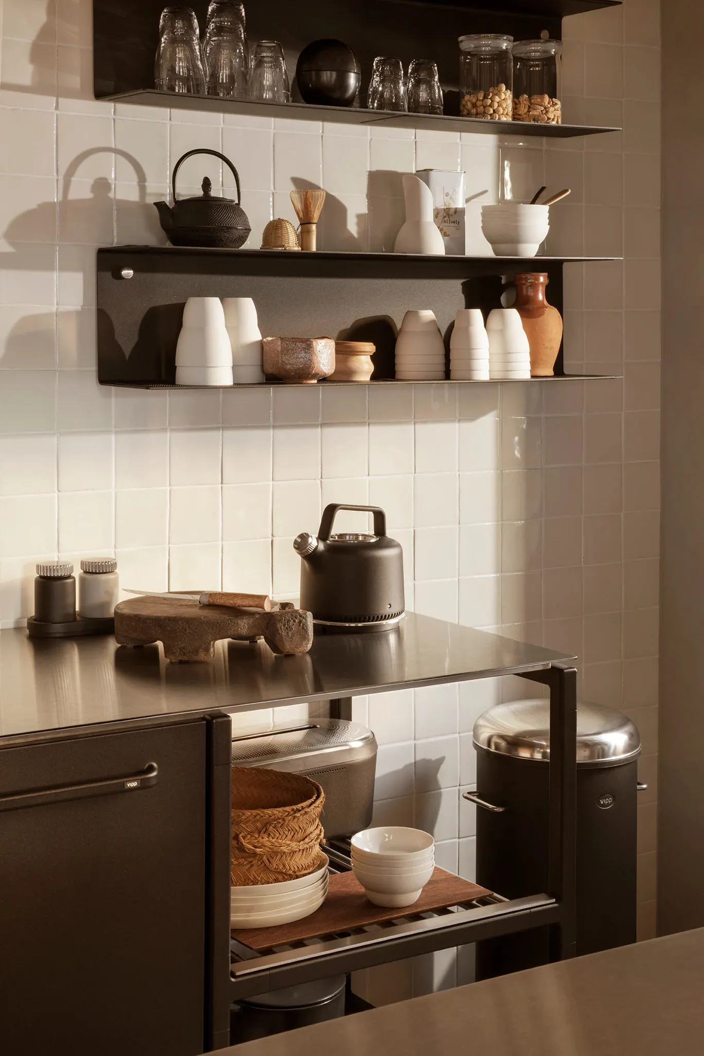 A minimalist residential kitchen featuring metal surfaces, white tiles, and organized shelving.