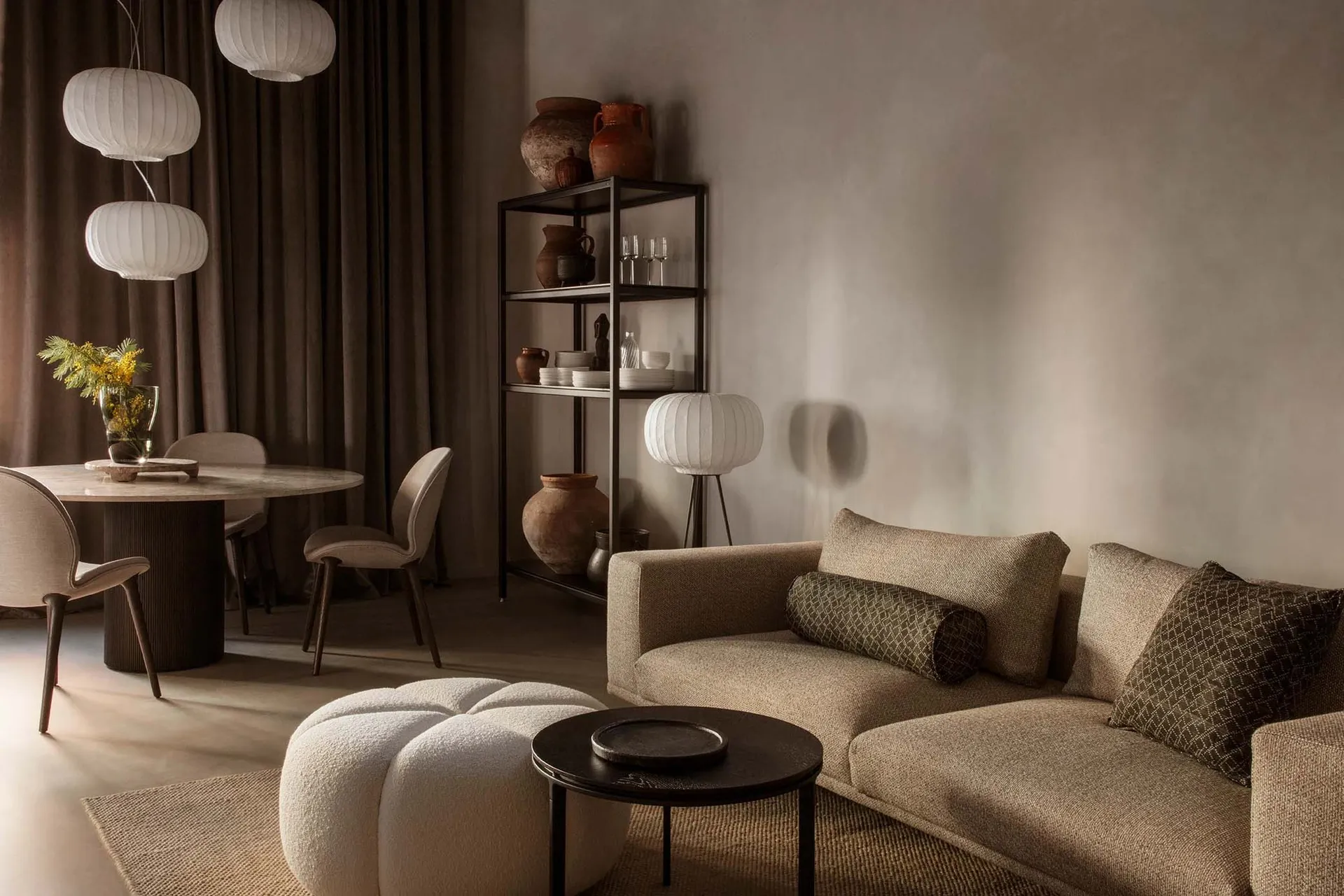A modern living room with neutral tones, featuring a couch, round table, and bookshelf.