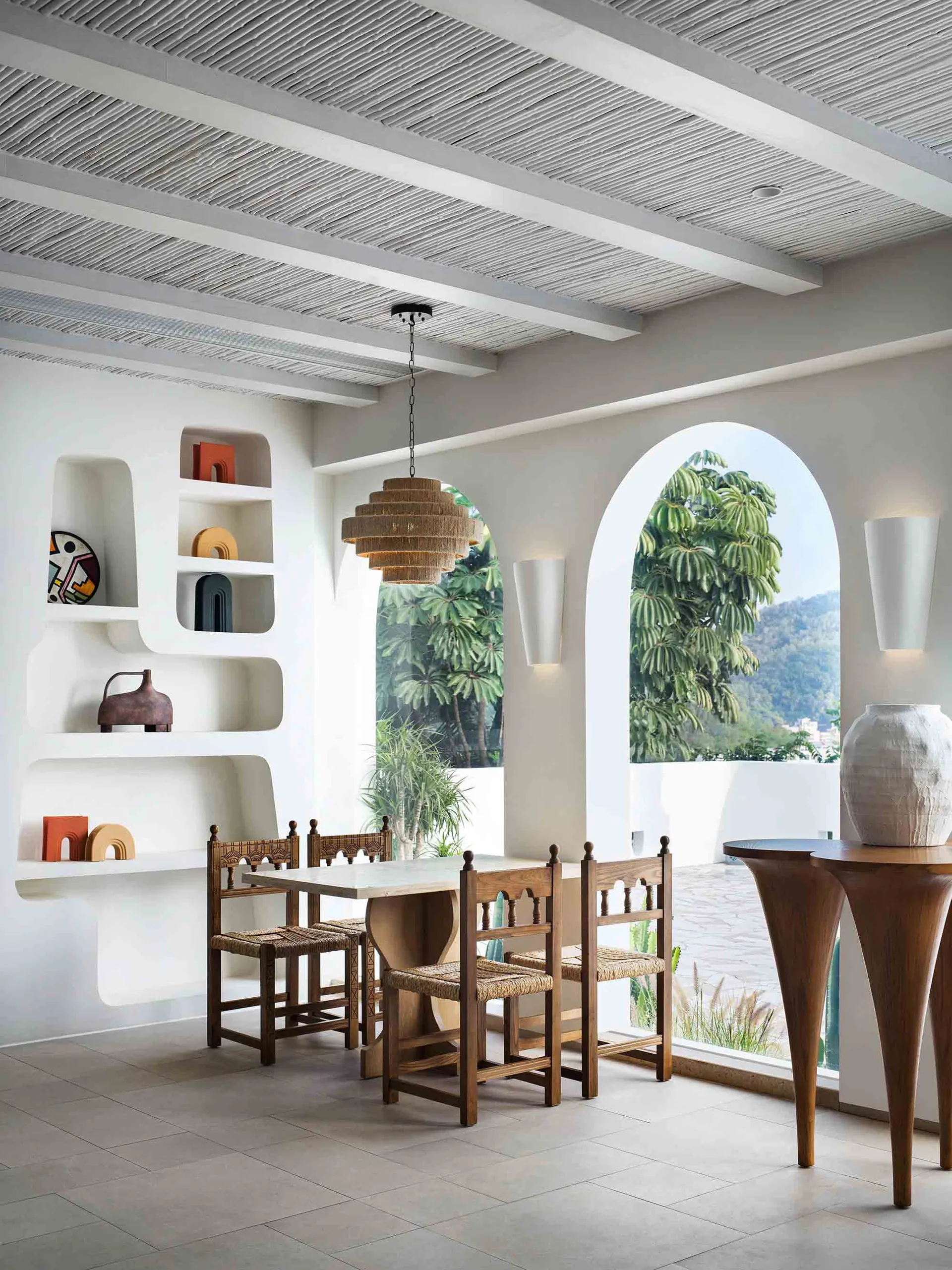 A minimalist dining room with concrete walls, wood furniture, and a modern chandelier.