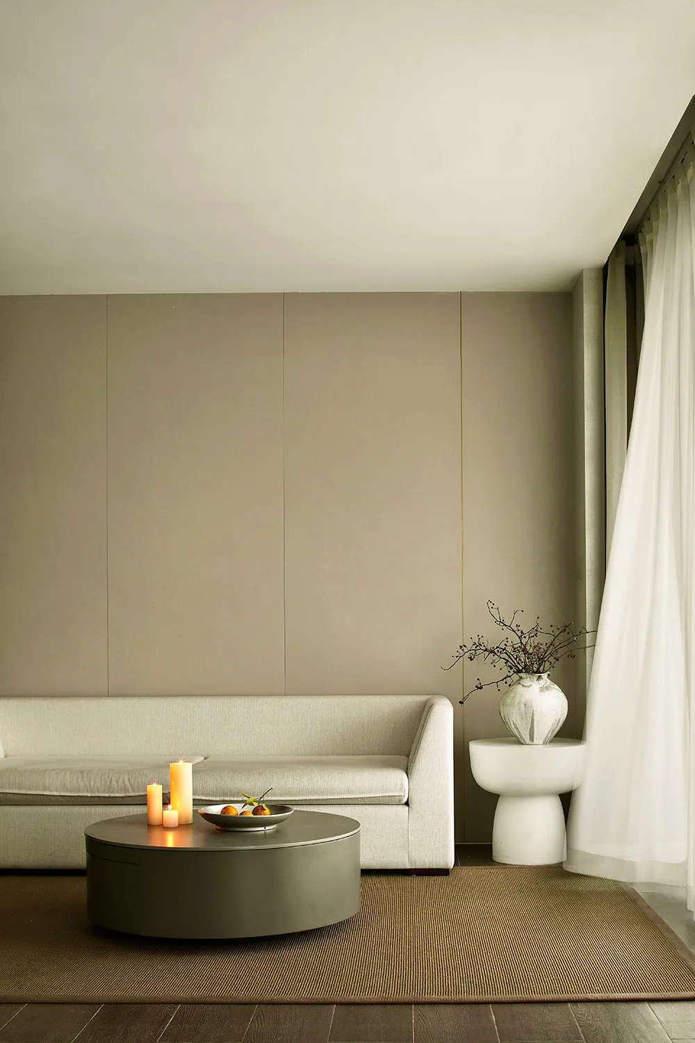 A minimalist living room with light-colored fabric furniture, a plain wooden floor, and a plain light-colored wall.