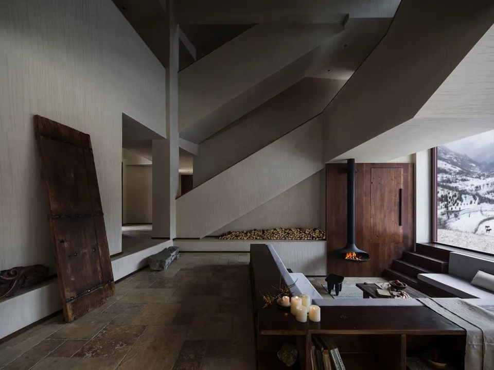 A minimalist living room with a wood floor, a wooden door, a fireplace, and a long low sofa.