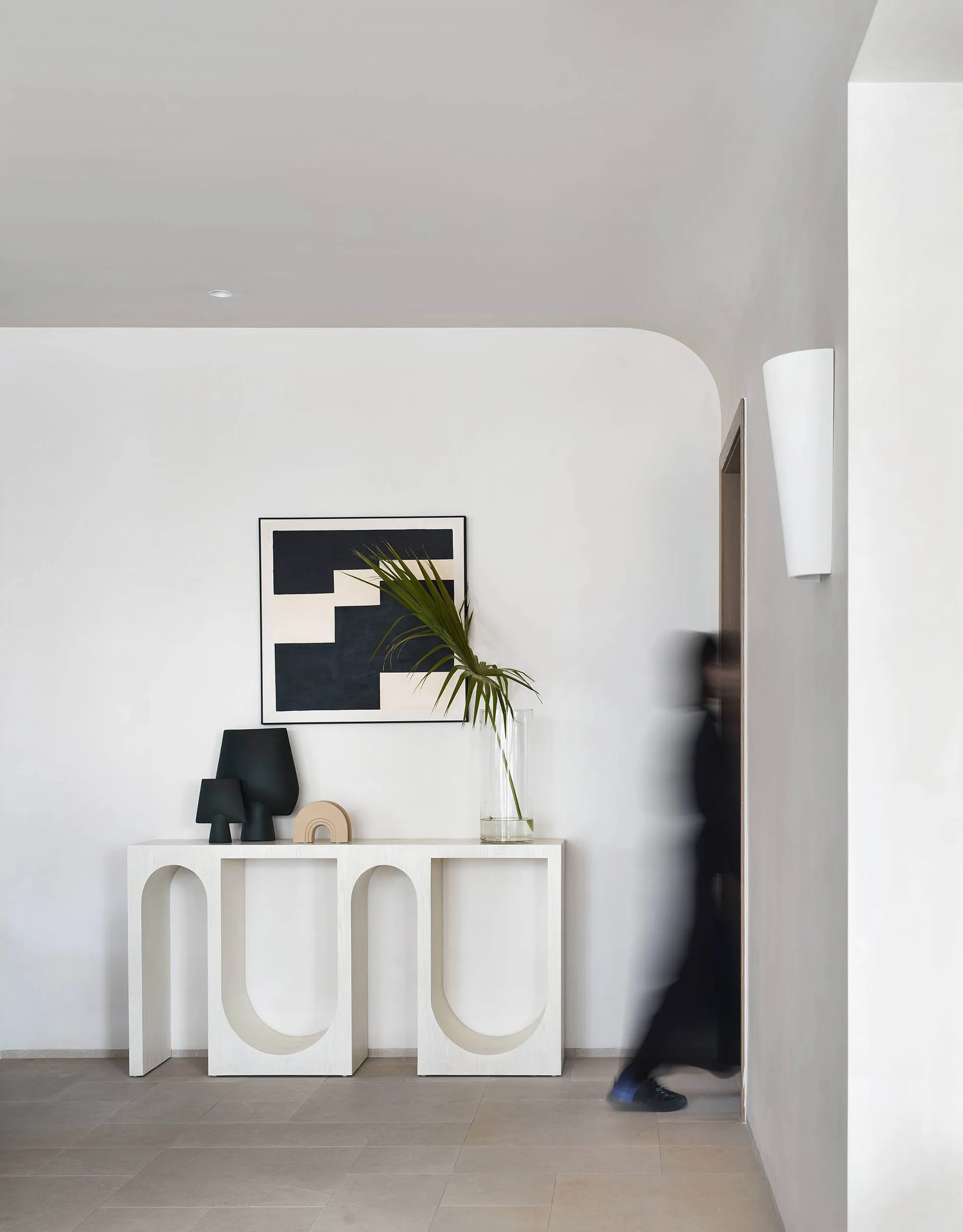 A minimalist entryway console table made of wood, featuring arch-shaped cutouts and a sleek, contemporary design, illuminated