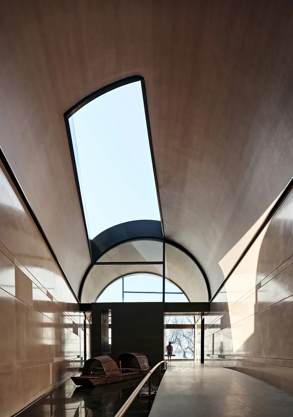 A modern architectural interior with a concrete ceiling and a skylight, featuring a boat-shaped sculpture on a polished floor