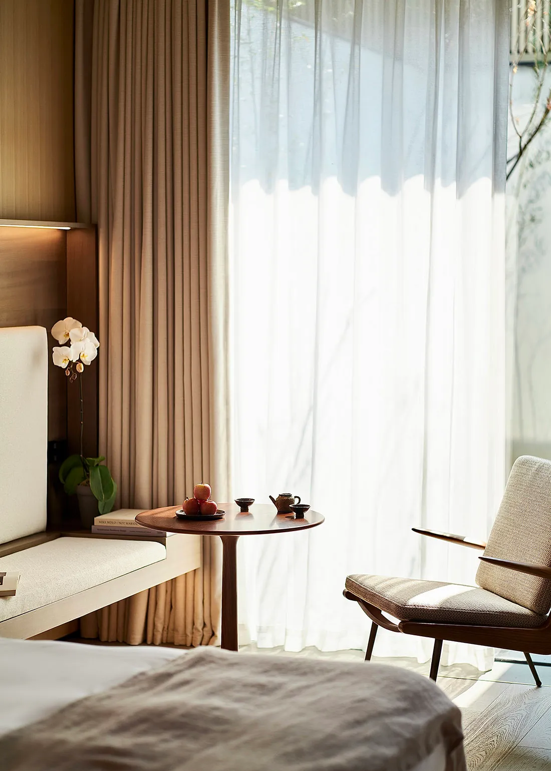 A modern minimalist bedroom featuring textured fabric upholstery, a small round table with a teapot and apples, and natural l