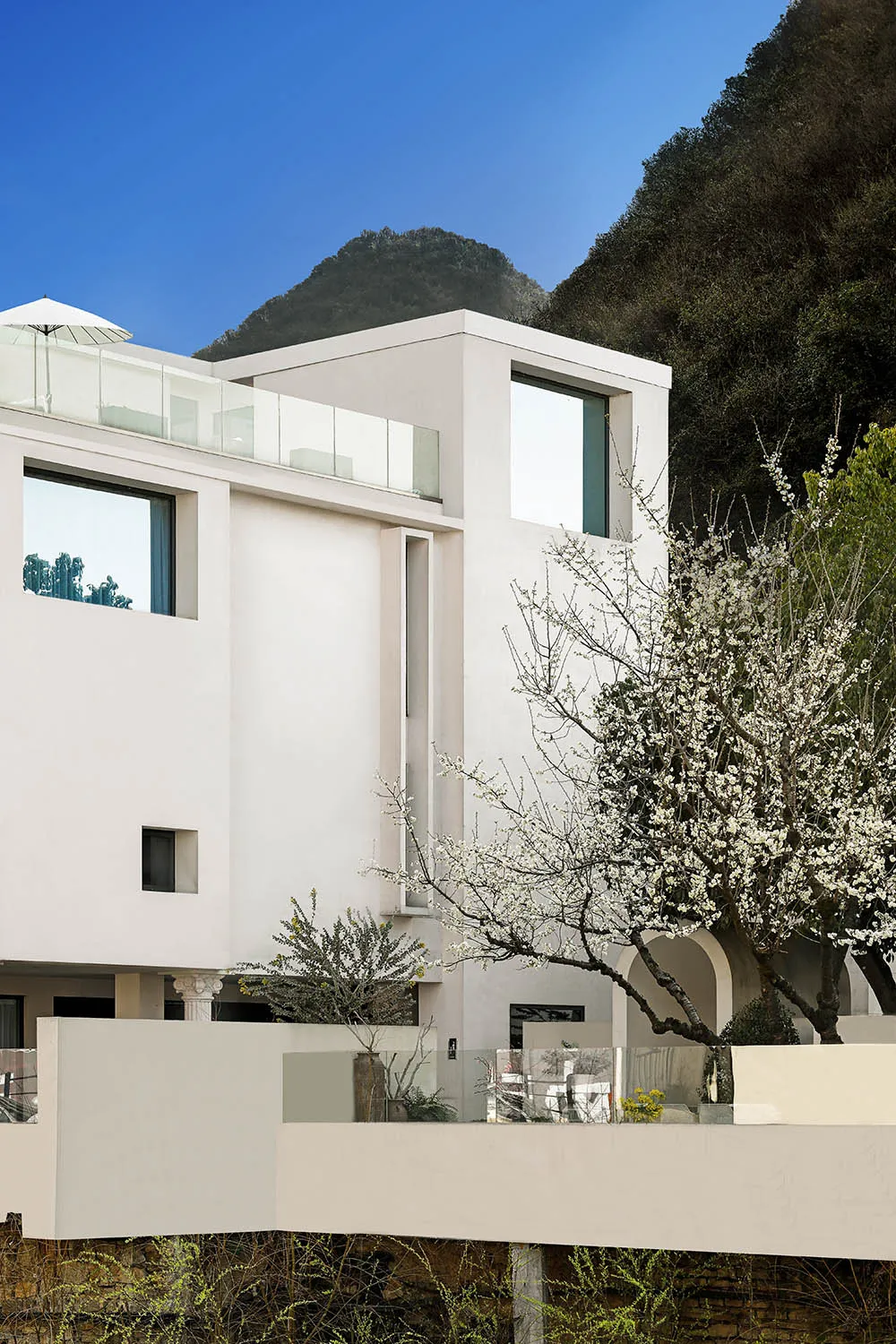 A modern residential building with a minimalist design, featuring concrete and glass materials, set against a mountainous bac