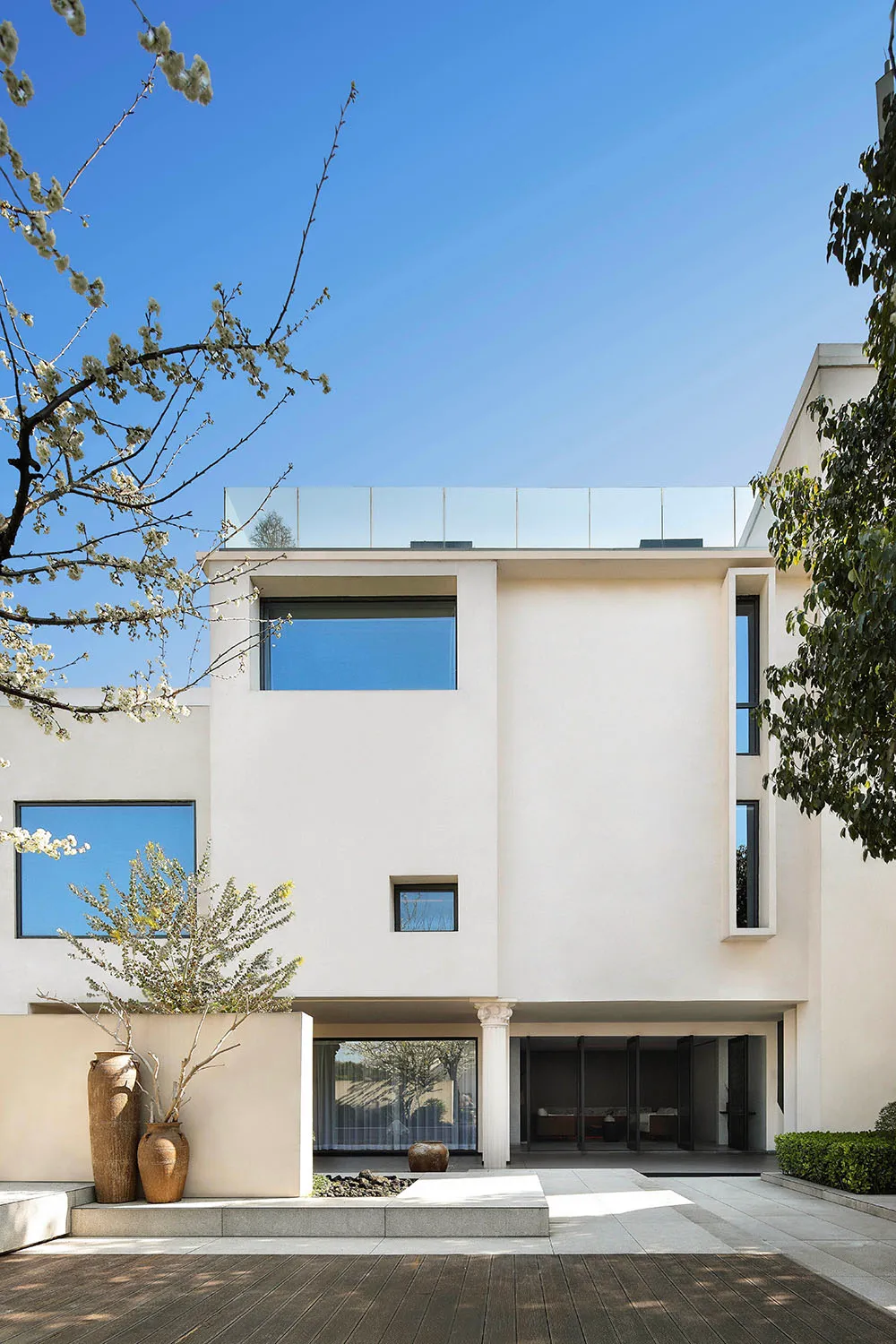 A modern residential house with white rendered concrete exterior and large glass windows.
