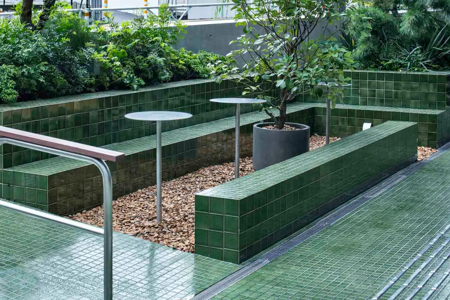 A landscaped area with green tiled benches, planters, and a few trees.