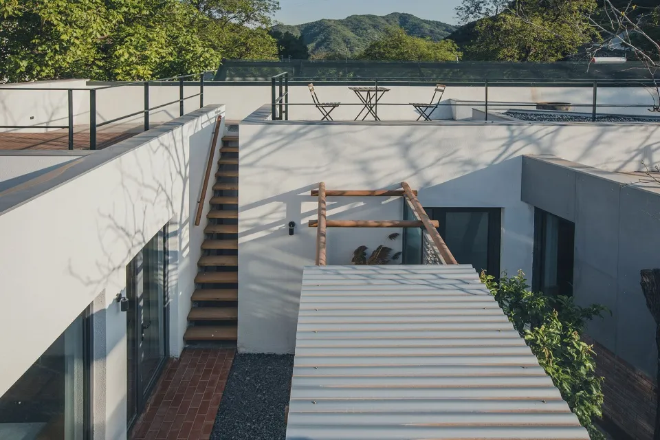 一棟極簡風格的金屬屋頂住宅，周圍環繞著樹木與山景。
