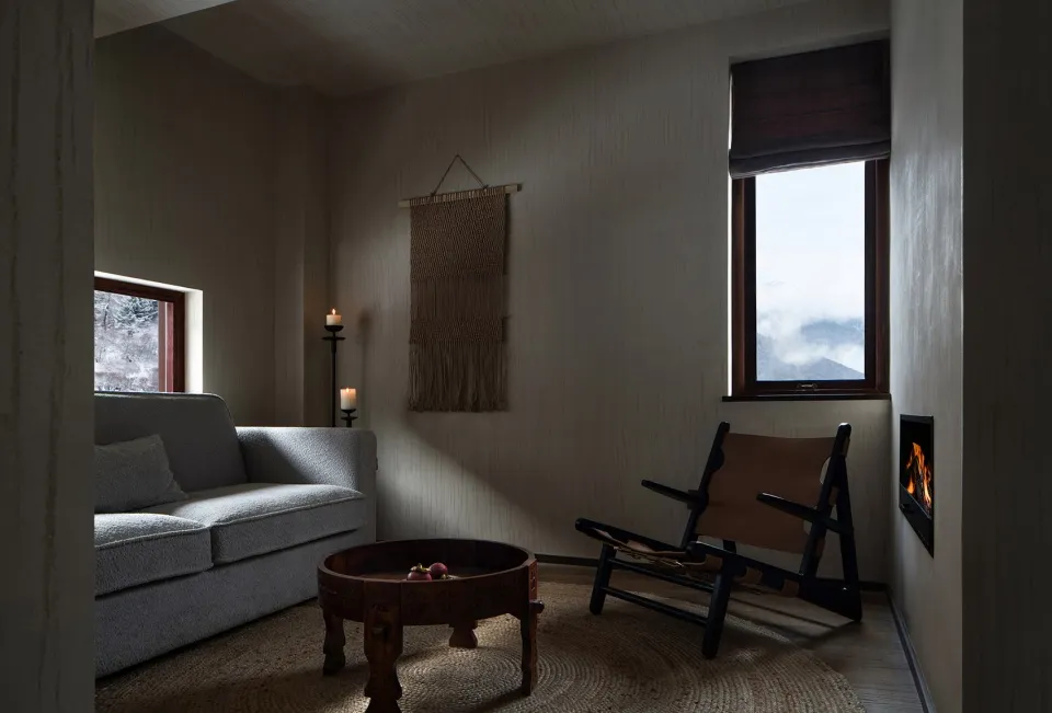 A modern living room with a gray couch, a wooden table, a leather chair, and a fireplace.