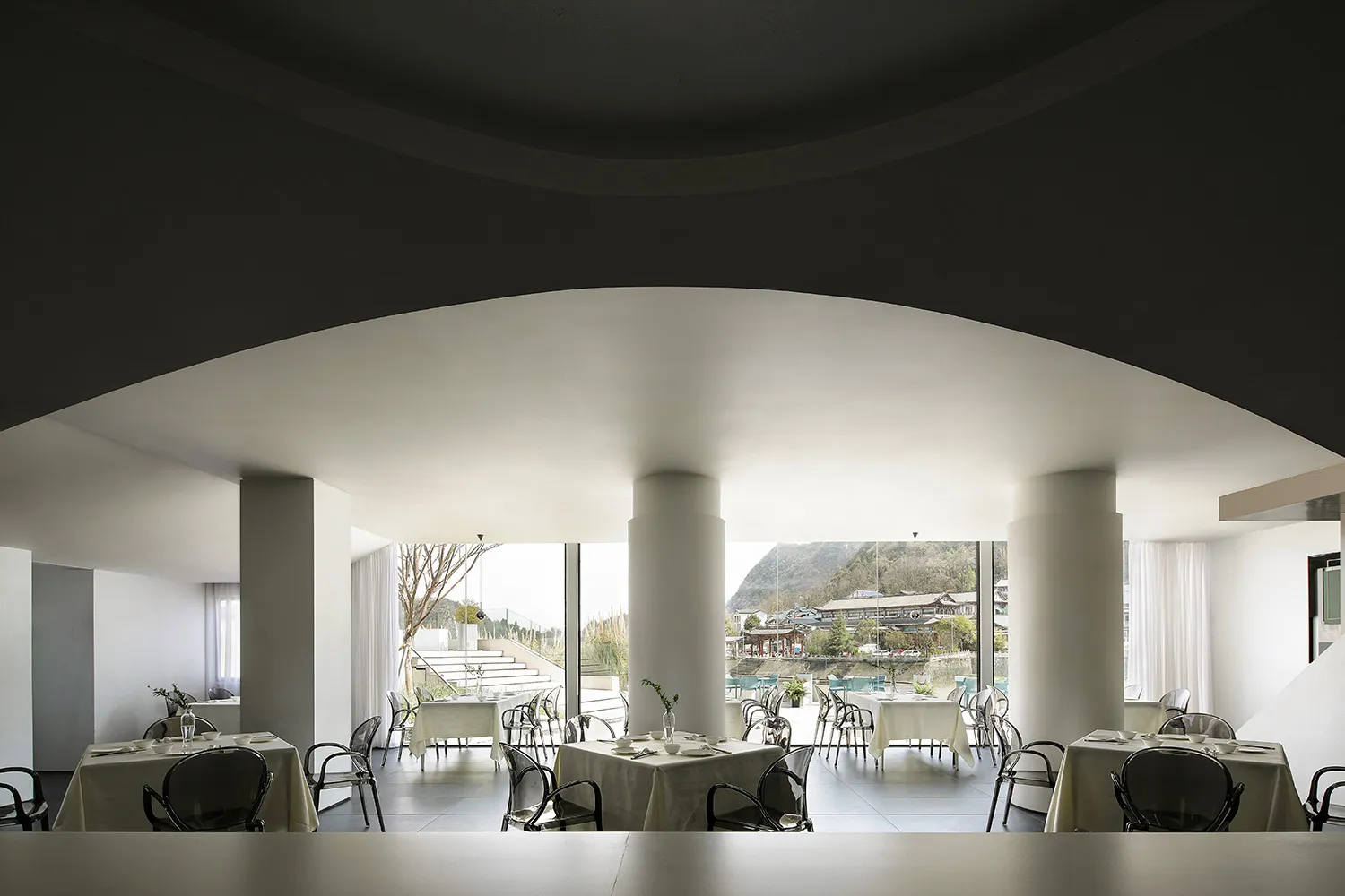 A sleek, modern restaurant interior with white stone flooring, white walls, and a minimalist design.
