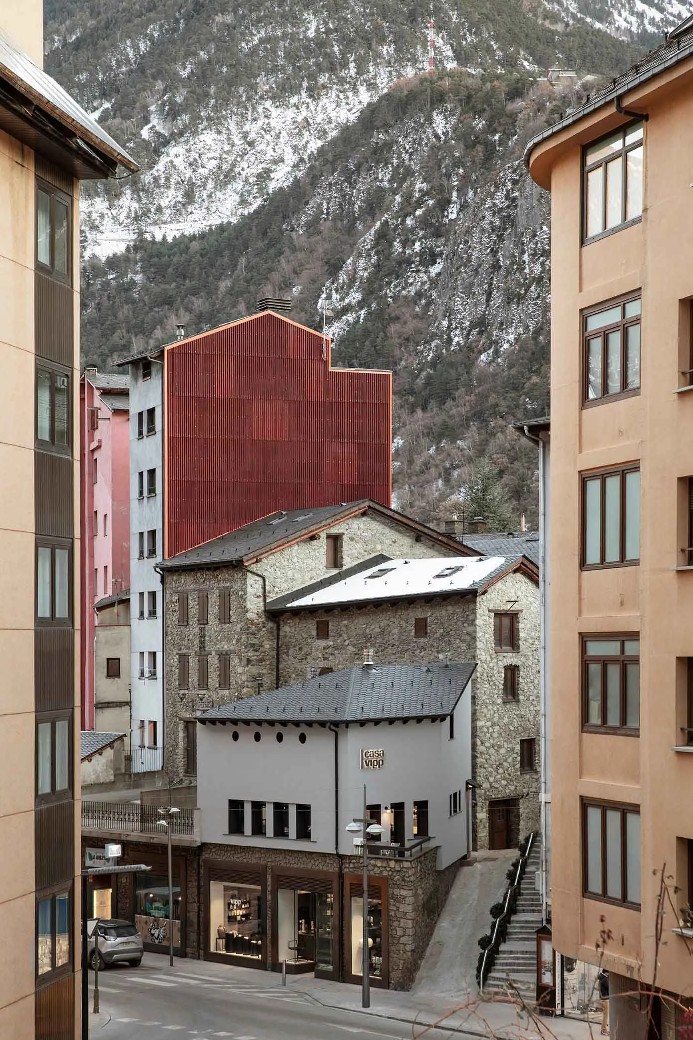 狹窄街道上的石材與混凝土建築,背景有現代紅色結構體。
