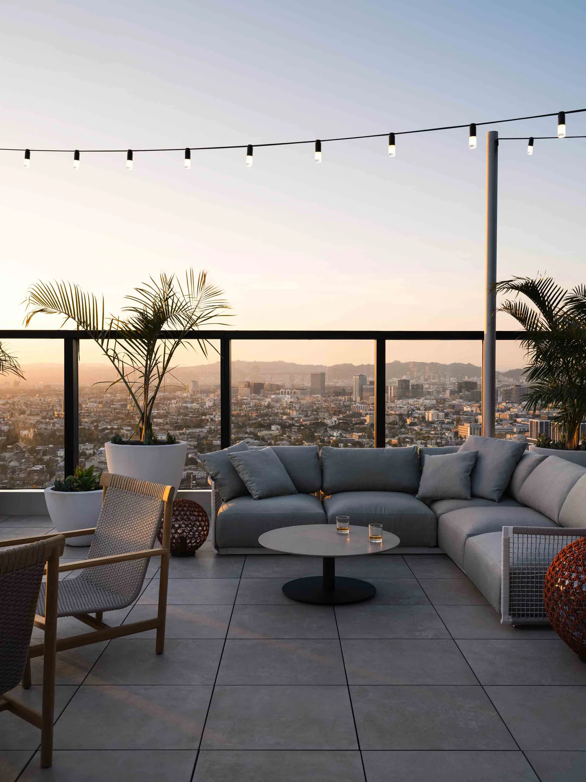 Outdoor rooftop lounge area with modern furniture, concrete floor, and hanging lights.