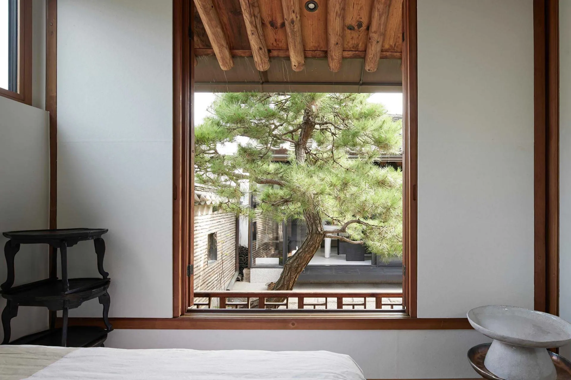 A minimalist window view of a traditional wooden house, showing a tree and a serene outdoor space.