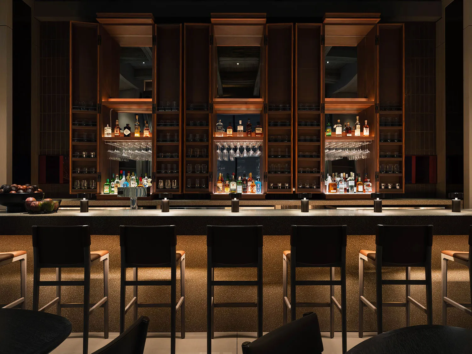 A modern bar counter with wooden elements, featuring a variety of bottles and glasses.