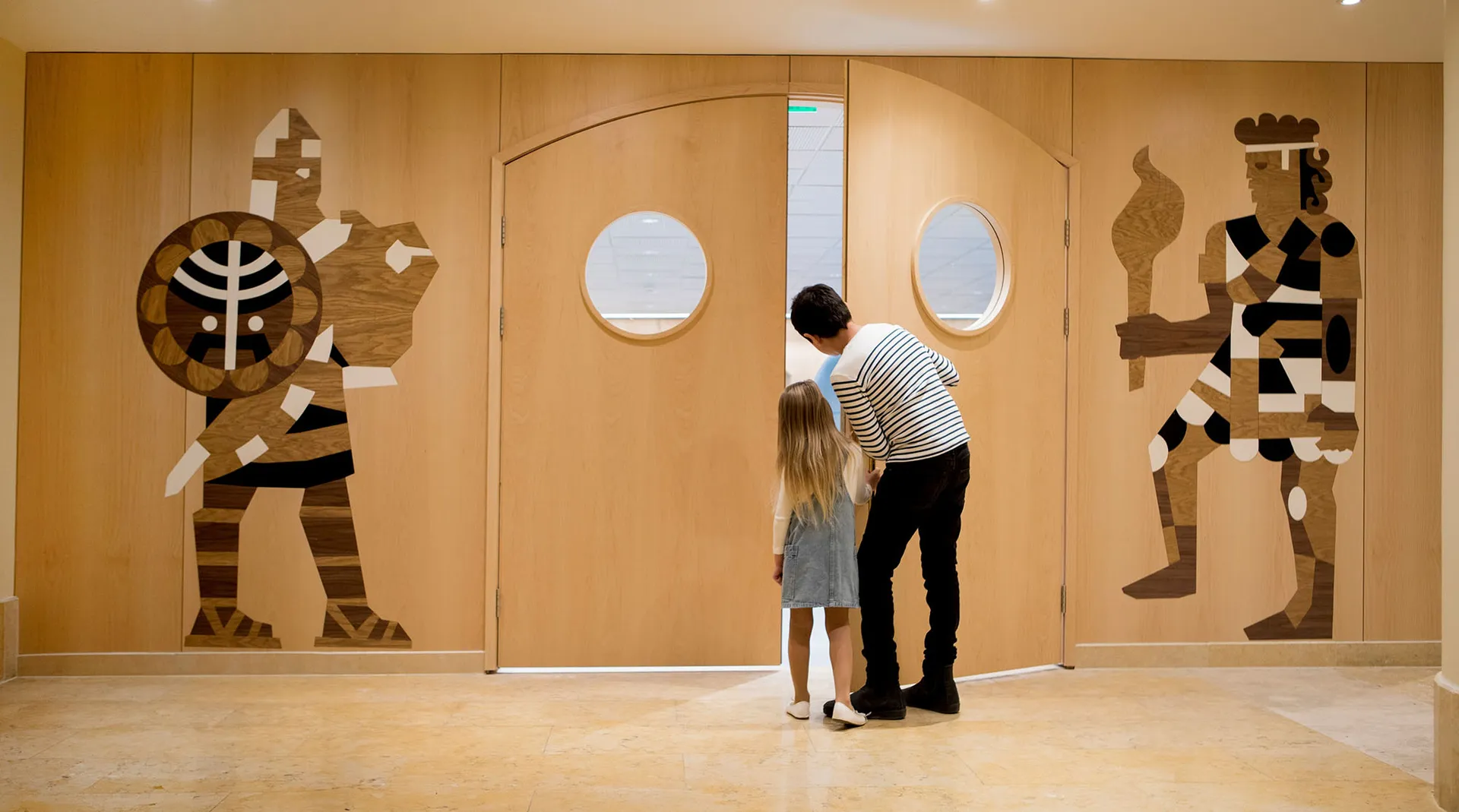 A modern entrance decorated with wood, featuring two wooden human-like figures.