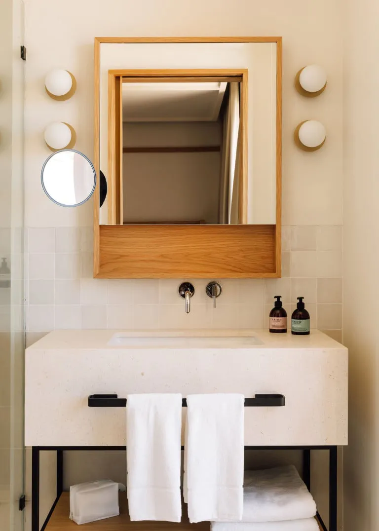 Modern minimalist bathroom featuring a sleek, concrete countertop with a built-in sink, white towels hanging below, and a mir