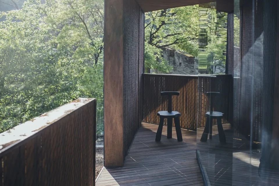 A modern outdoor wooden balcony with greenery in the background.
