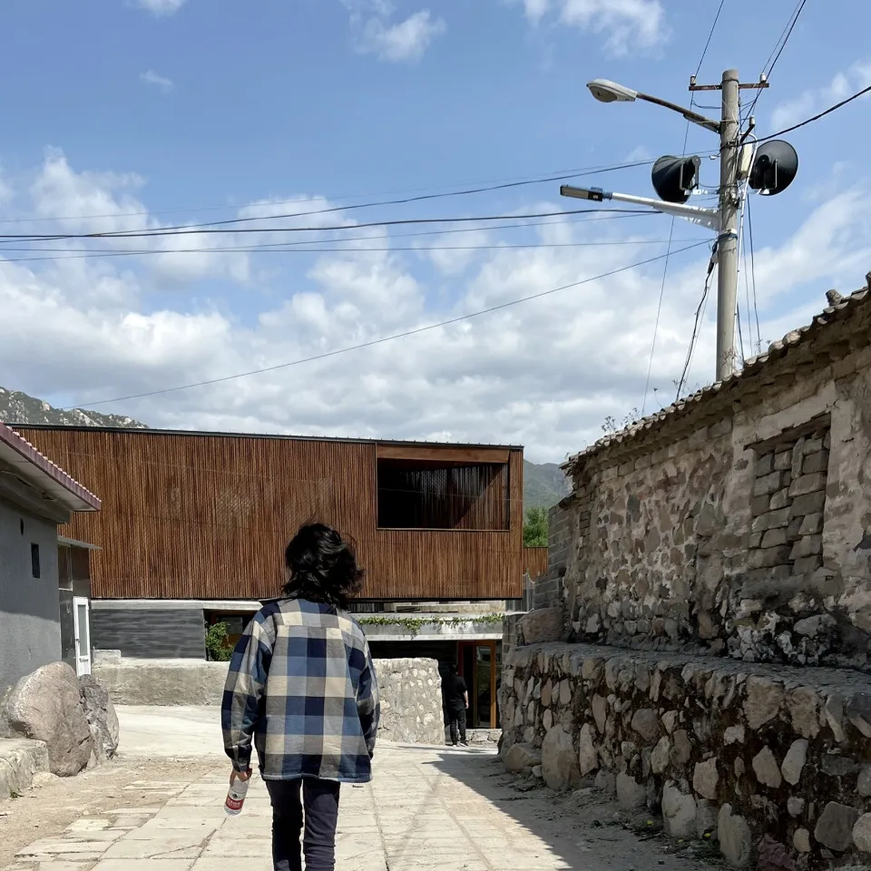 一位行人走在街道上,背景是一棟木造建築。