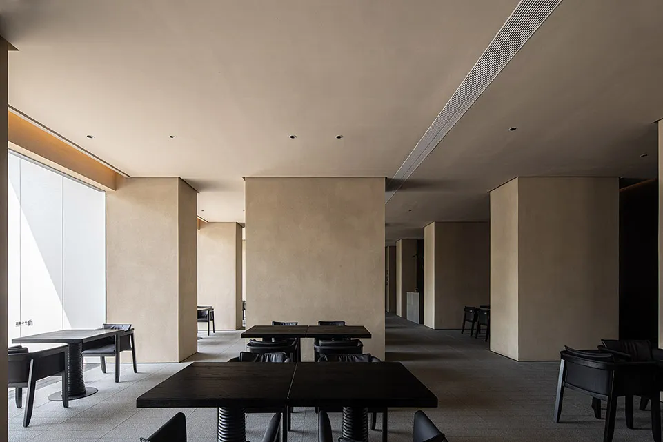 A minimalistic restaurant interior featuring concrete walls and metal tables and chairs.