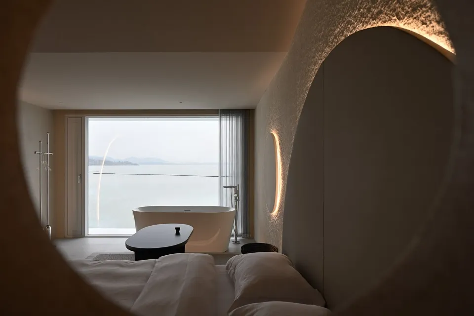 A modern bedroom featuring a concrete floor, glass walls, and minimalist decor.