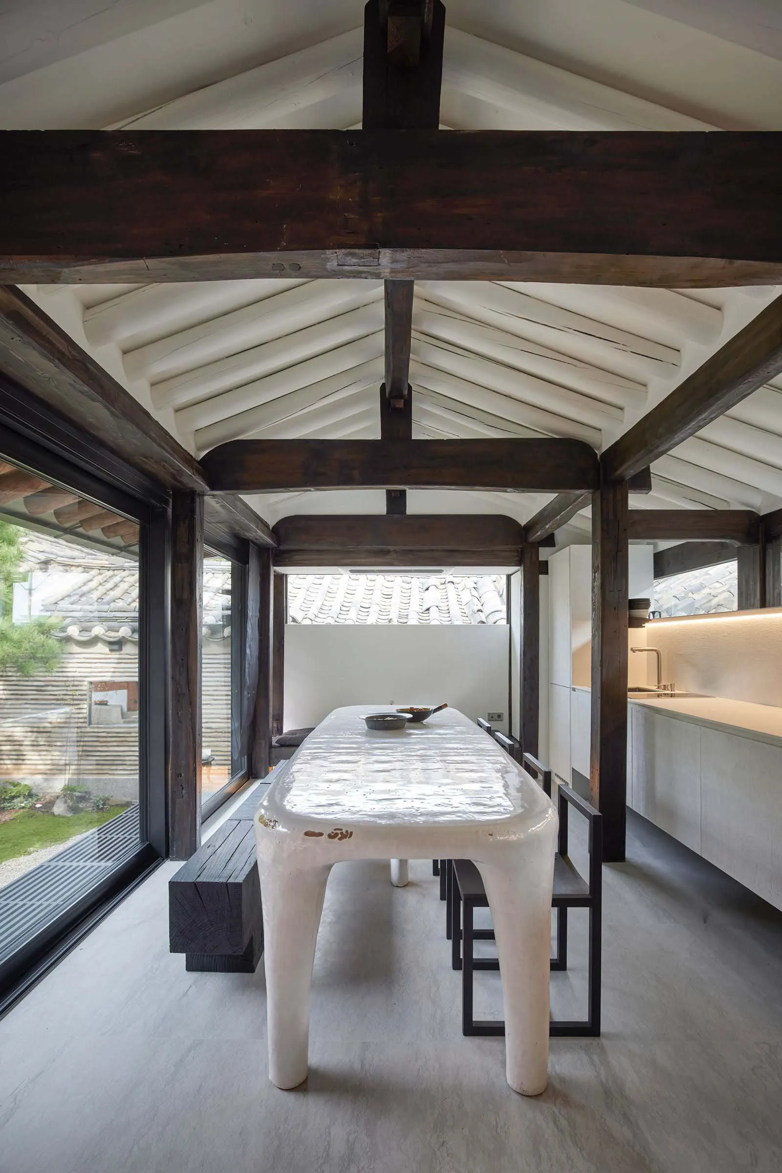 A modern dining room featuring a sleek, white ceramic dining table and black bench seating.