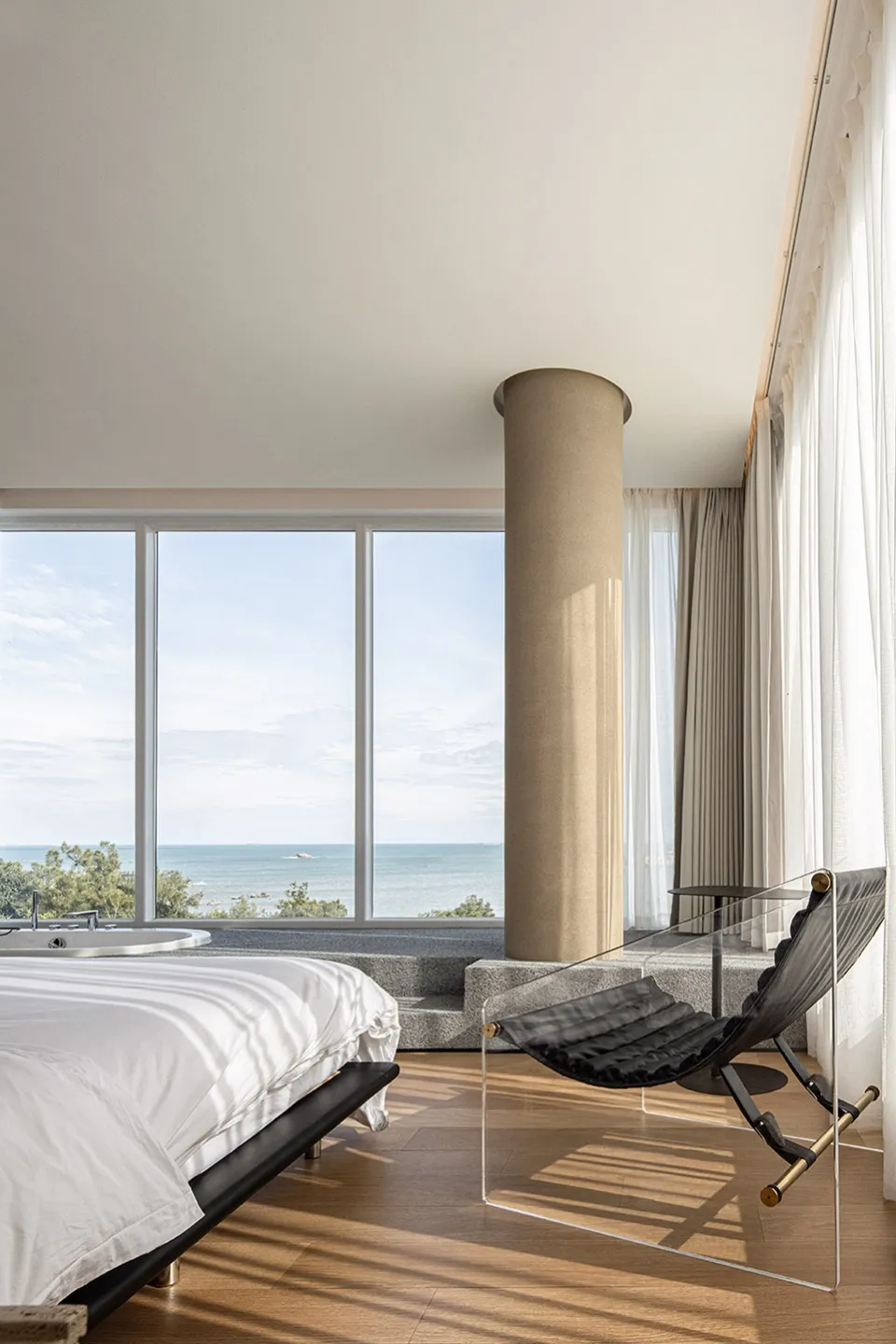 A modern minimalist bedroom with a glass wall overlooking the ocean.