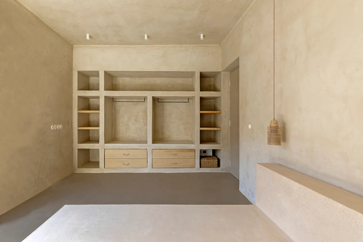 A minimalist closet with concrete walls and floor, featuring built-in shelves and wooden drawers.