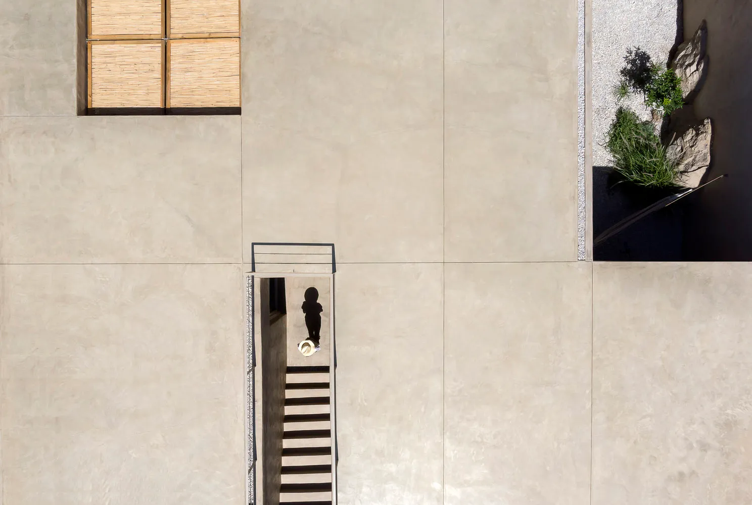 A minimalist staircase constructed from concrete, viewed from above with a person standing at the bottom.
