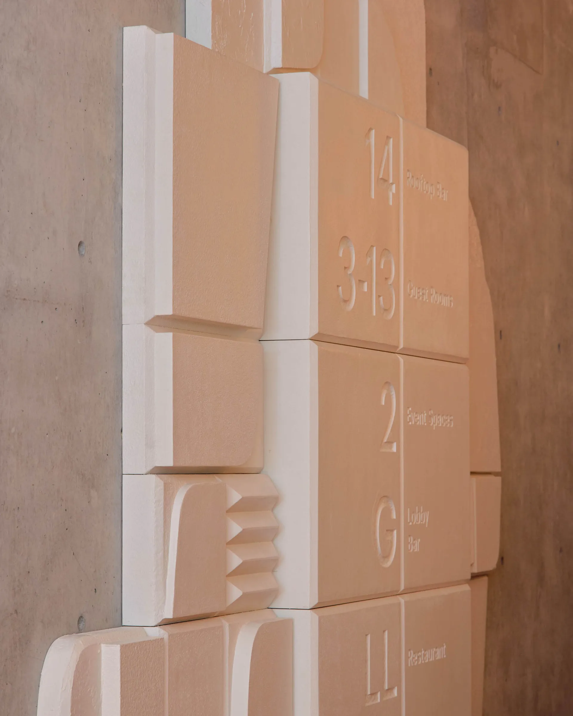 A wall of beige concrete cubes with numbers and labels indicating different levels and areas of a building.