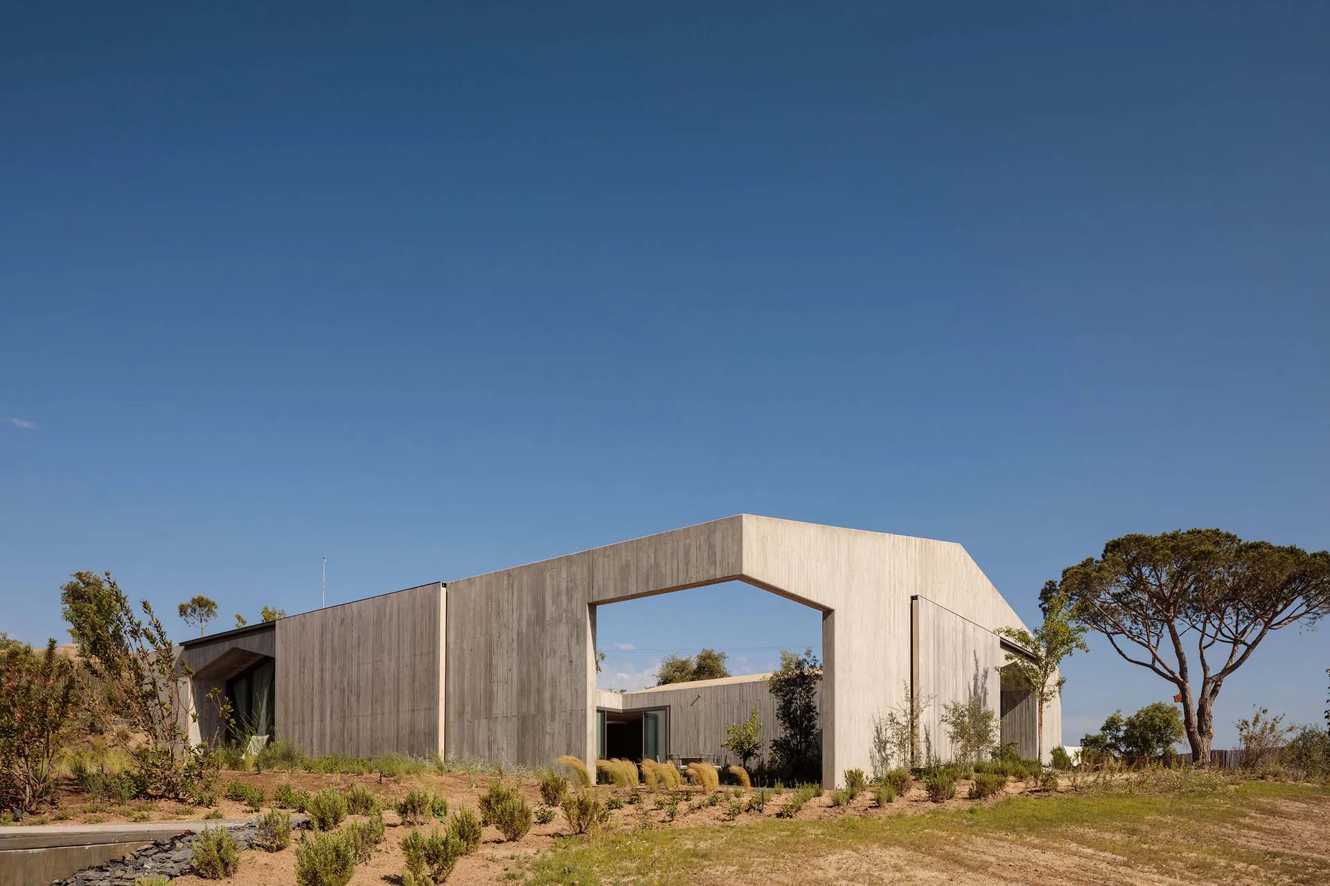 A modern residential building with a concrete exterior and a large arched opening on a clear, sunny day.