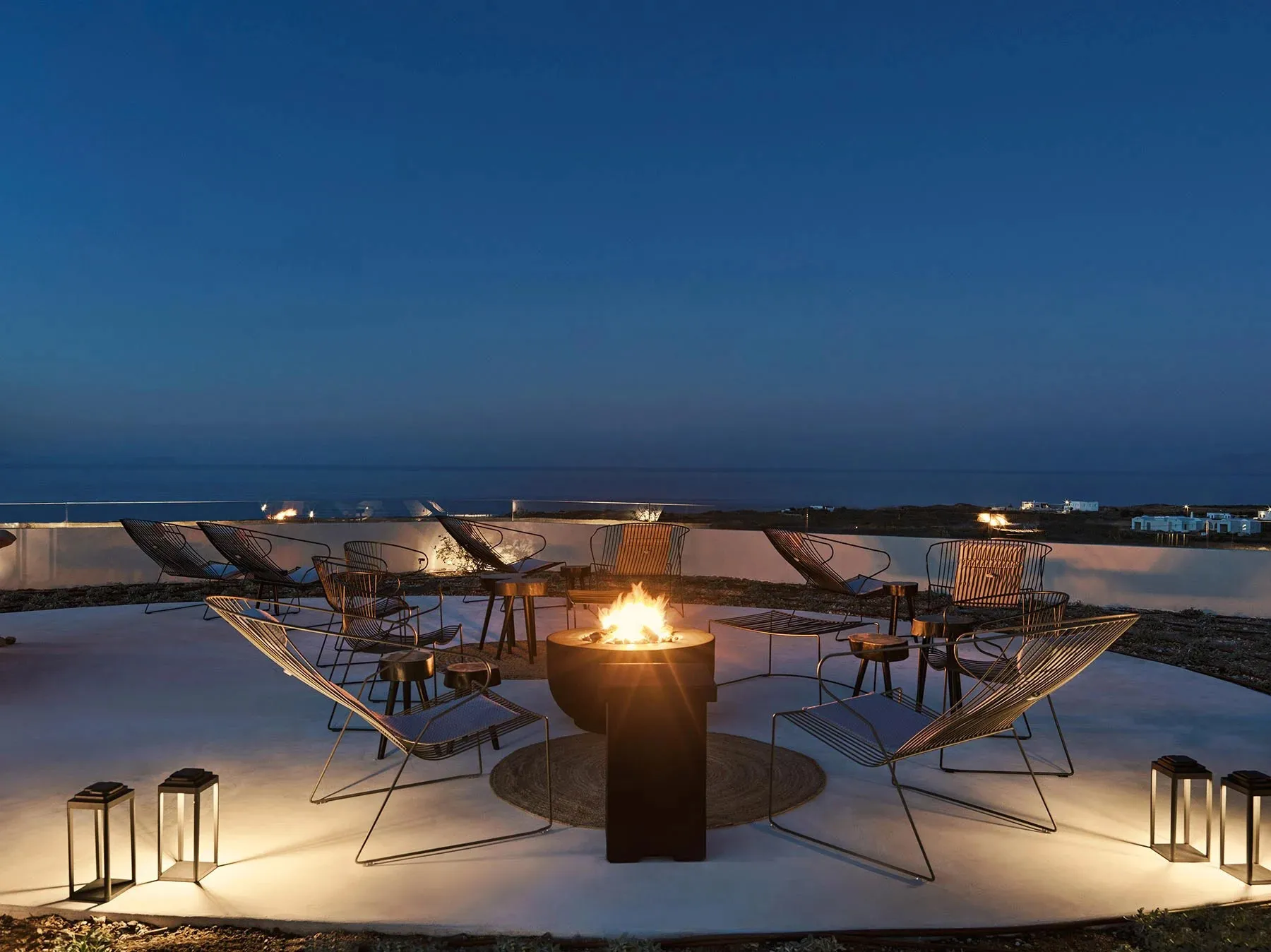 Industrial-style outdoor lounge with metal chairs and a fire pit at night.