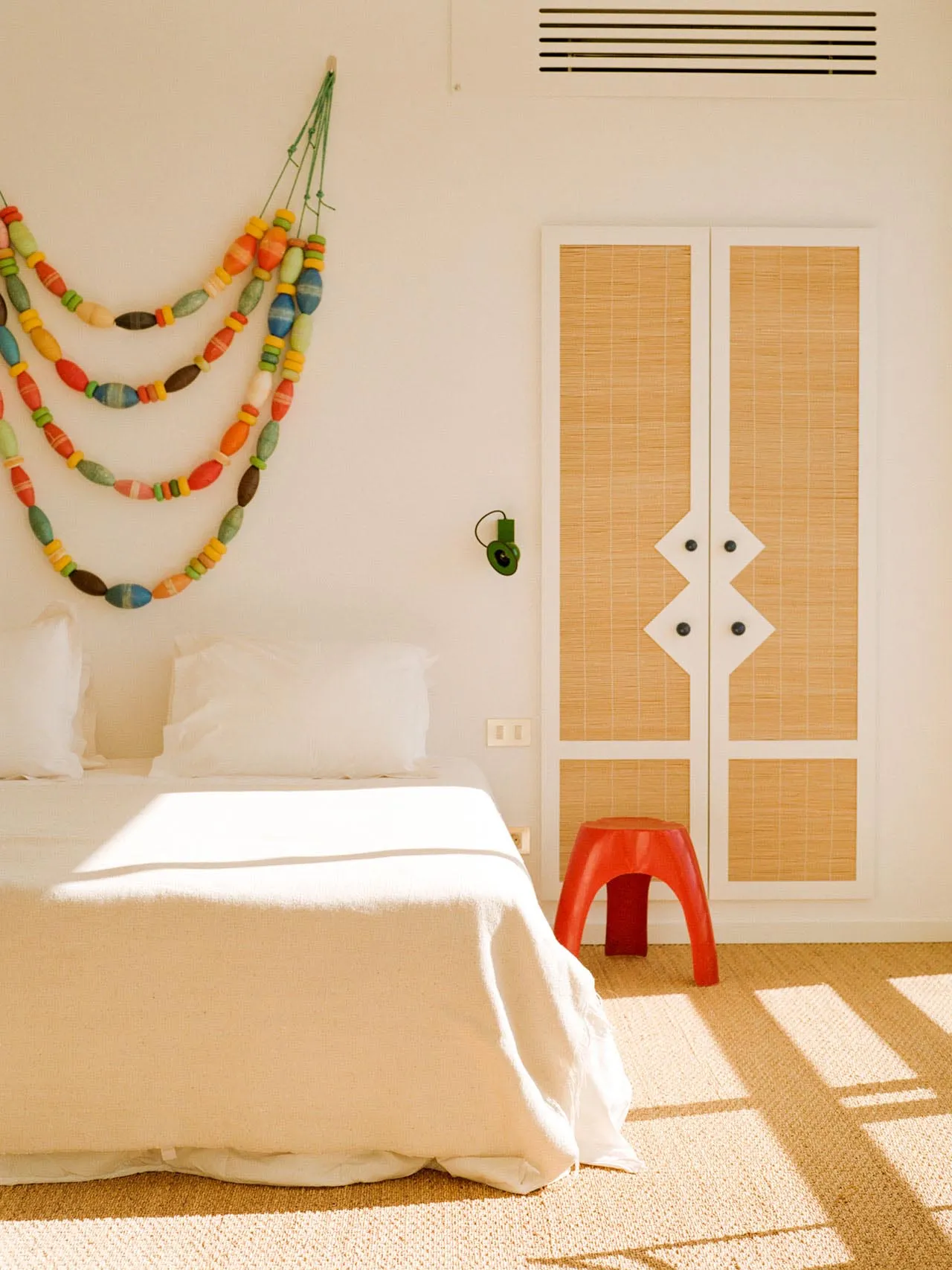 A minimalist bedroom with a bed covered in a white sheet and pillows, adorned with a colorful beaded garland hanging on the w