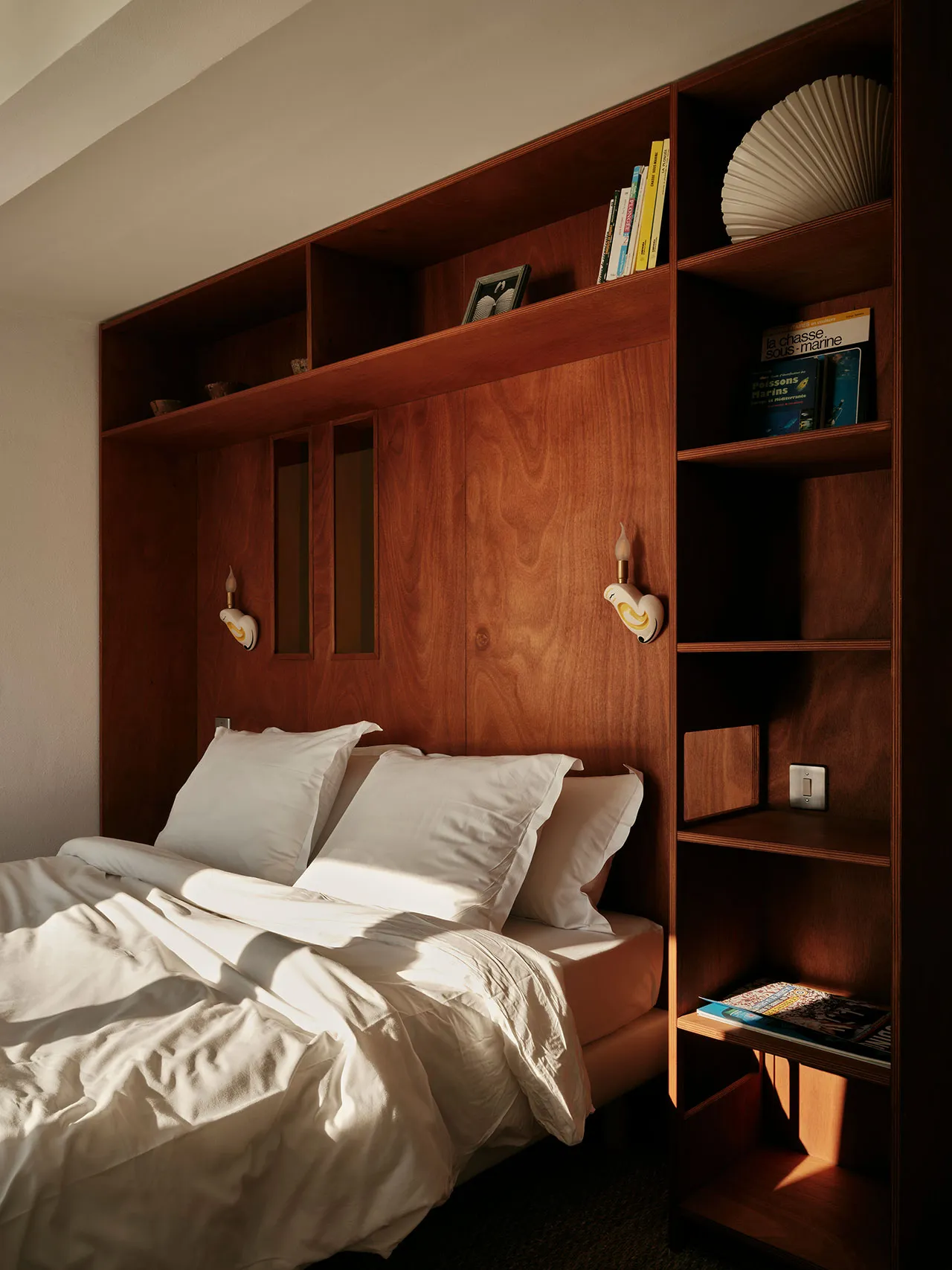 A minimalist bedroom featuring a wooden bookshelf with built-in lighting and storage.