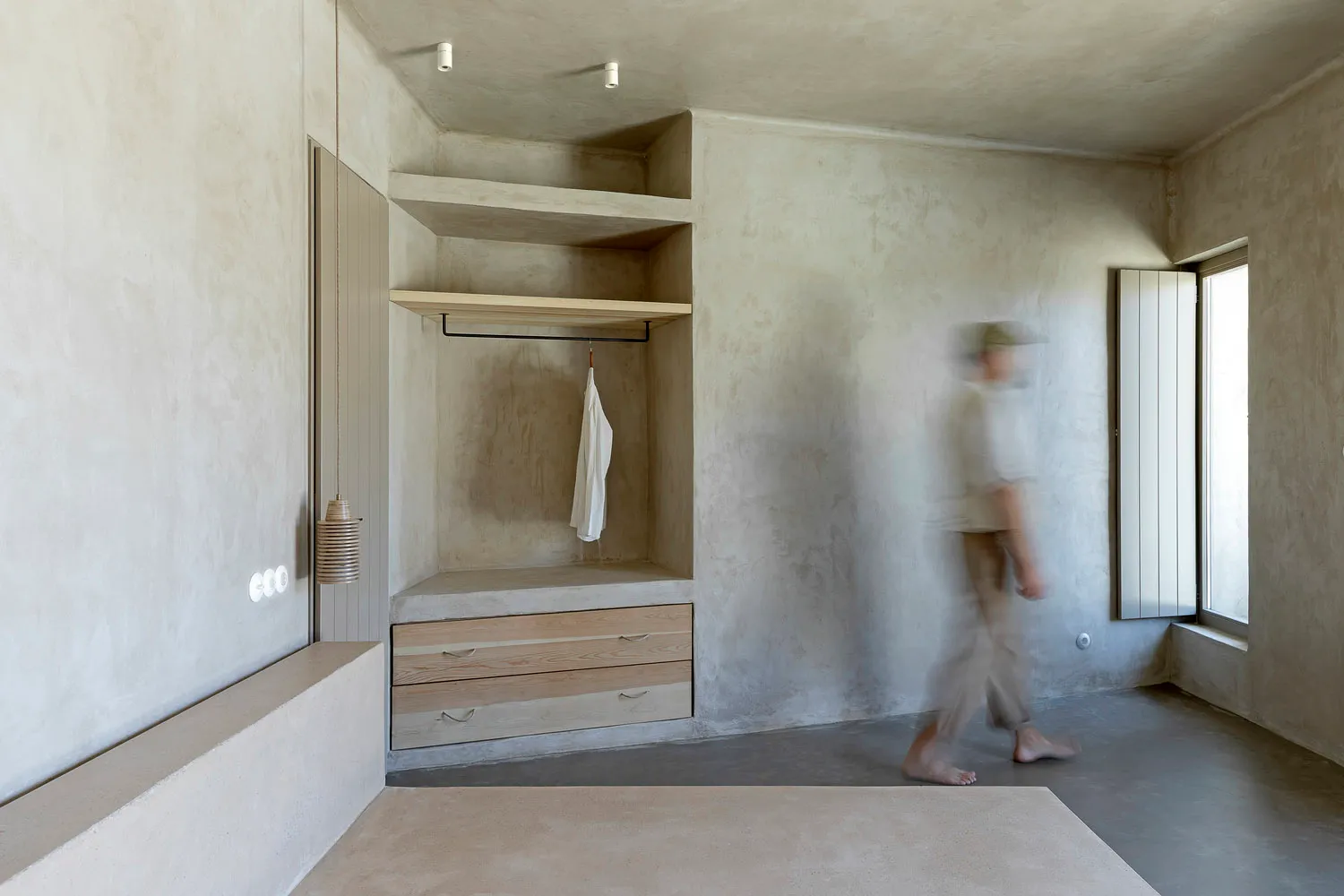 A minimalist concrete wardrobe with a white shirt hanging on a clothes rail.