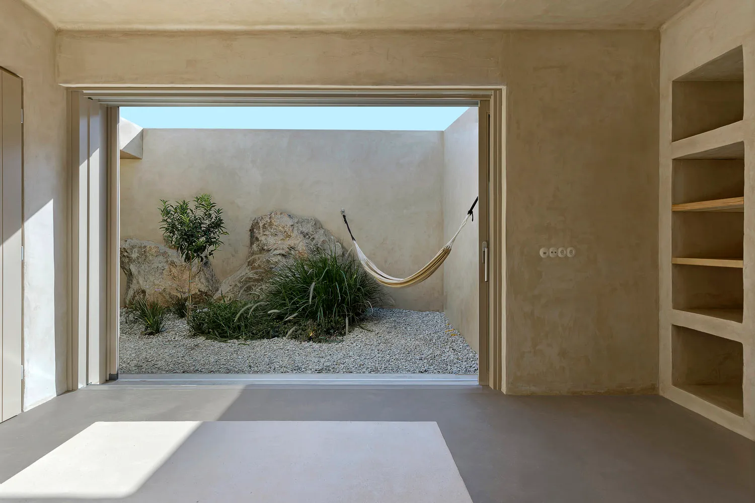 Minimalist-style indoor garden with concrete walls, rocks, and a hammock.